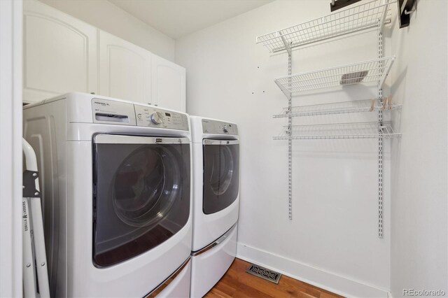 washroom with visible vents, dark wood-style floors, cabinet space, baseboards, and washing machine and clothes dryer