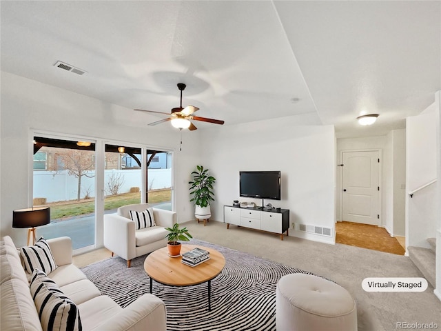 living area featuring carpet floors, visible vents, stairway, and a ceiling fan