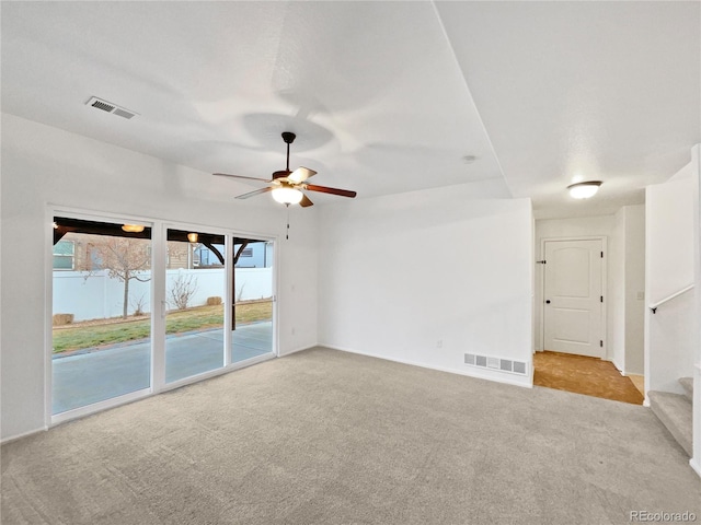 unfurnished room with carpet, visible vents, ceiling fan, and stairs