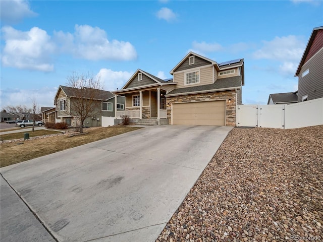 view of front of house with driveway, stone siding, an attached garage, a gate, and roof mounted solar panels