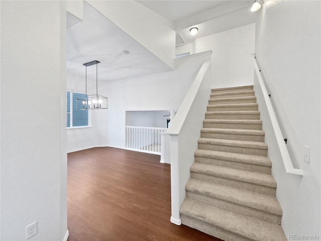 stairway featuring a notable chandelier, baseboards, and wood finished floors