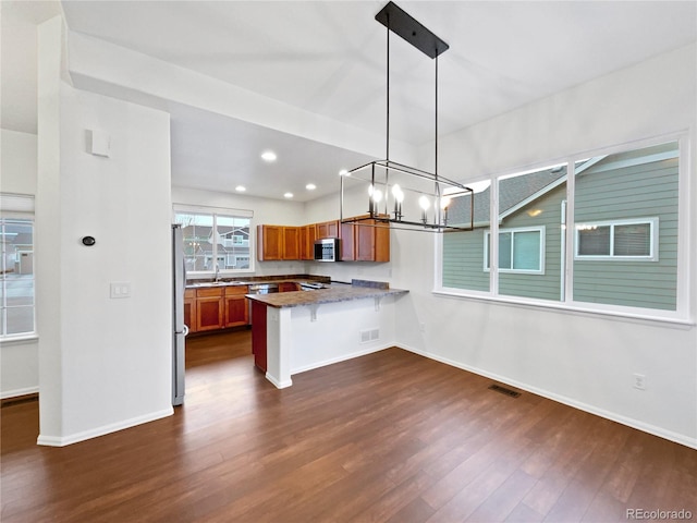 kitchen with visible vents, appliances with stainless steel finishes, brown cabinets, dark wood-style flooring, and a peninsula