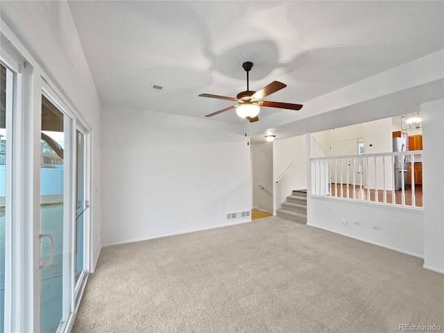 carpeted spare room featuring a ceiling fan, visible vents, and stairs