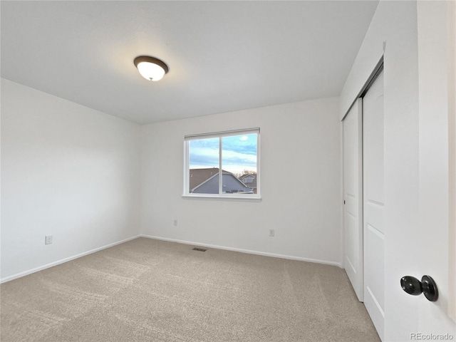 unfurnished bedroom with a closet, light colored carpet, visible vents, and baseboards