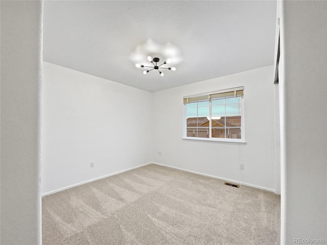 carpeted spare room with baseboards, visible vents, and a notable chandelier