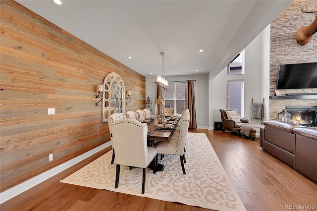 dining area featuring hardwood / wood-style flooring, wooden walls, and a stone fireplace