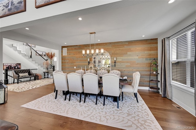 dining room with a notable chandelier, wooden walls, and hardwood / wood-style floors