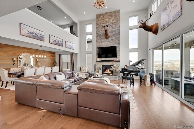 living room with a towering ceiling, light wood-type flooring, a notable chandelier, and a fireplace