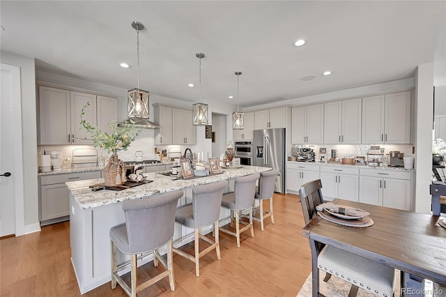 kitchen featuring pendant lighting, backsplash, a kitchen island with sink, light hardwood / wood-style floors, and stainless steel appliances