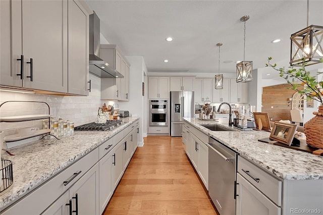 kitchen featuring appliances with stainless steel finishes, wall chimney exhaust hood, decorative light fixtures, decorative backsplash, and sink