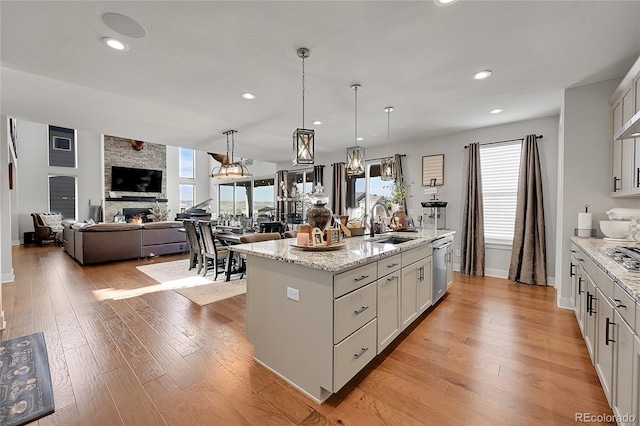 kitchen with a fireplace, white cabinetry, decorative light fixtures, light stone counters, and a center island with sink