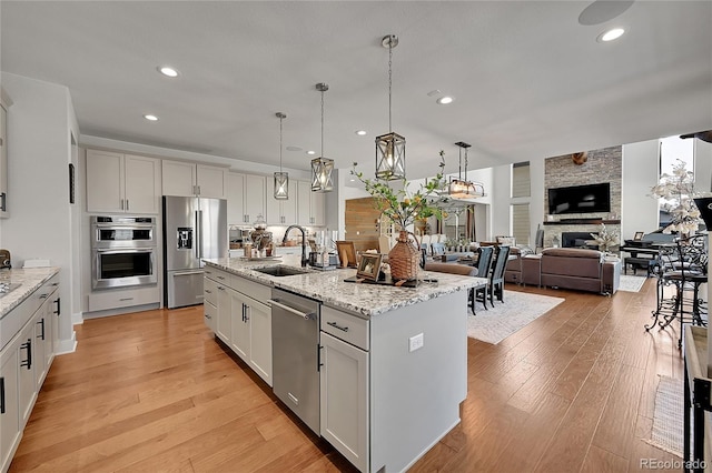 kitchen with appliances with stainless steel finishes, sink, white cabinetry, a fireplace, and a kitchen island with sink