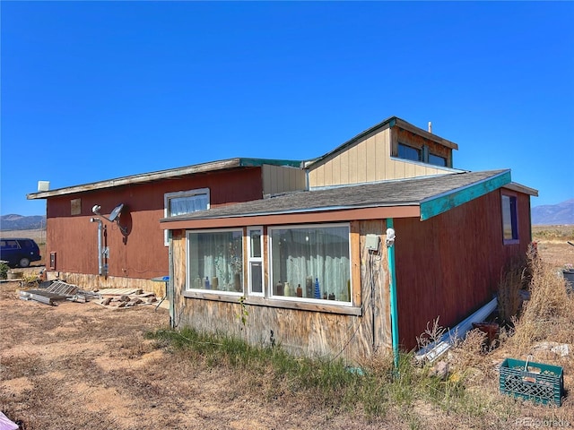 view of side of property with a mountain view and a shingled roof