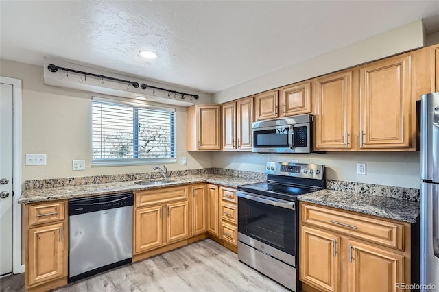 kitchen with sink, rail lighting, light stone counters, light hardwood / wood-style flooring, and appliances with stainless steel finishes