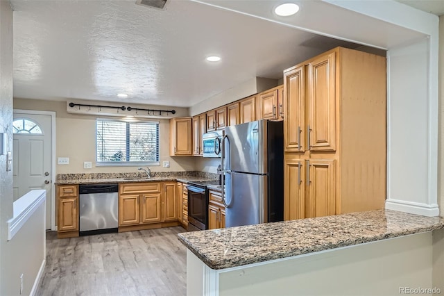 kitchen featuring kitchen peninsula, stainless steel appliances, sink, stone counters, and light hardwood / wood-style floors