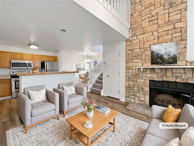 living room with a notable chandelier, a stone fireplace, and light hardwood / wood-style flooring