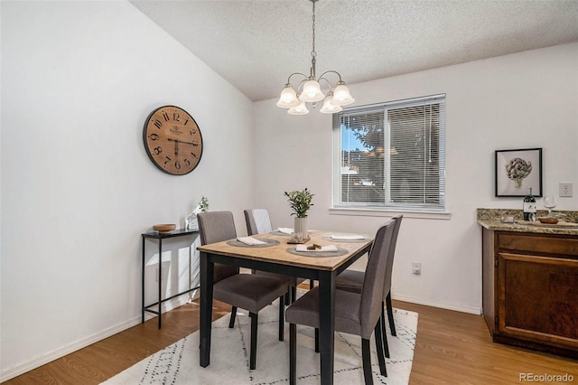 dining room with vaulted ceiling, a textured ceiling, a chandelier, and light hardwood / wood-style flooring