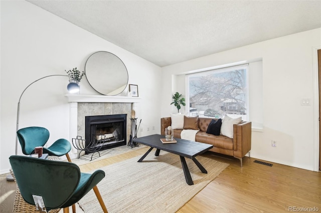 living room with wood-type flooring, a tile fireplace, a textured ceiling, and vaulted ceiling