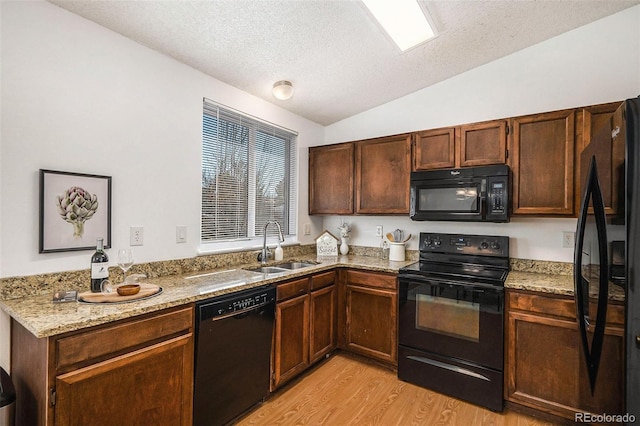 kitchen featuring lofted ceiling, sink, light stone counters, light hardwood / wood-style flooring, and black appliances