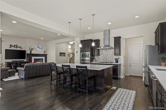 kitchen with decorative backsplash, appliances with stainless steel finishes, wall chimney range hood, decorative light fixtures, and a center island