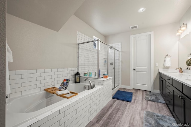 full bathroom with double vanity, a bath, visible vents, a stall shower, and wood finished floors
