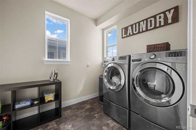laundry area with laundry area, baseboards, washing machine and dryer, and a healthy amount of sunlight