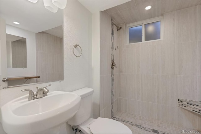 bathroom featuring sink, a tile shower, and toilet