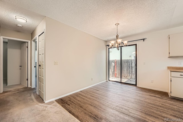 unfurnished dining area featuring a textured ceiling, a chandelier, baseboards, and wood finished floors