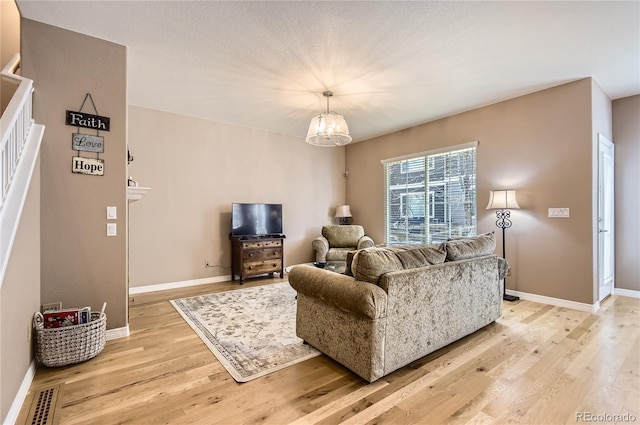 living room with light wood finished floors, baseboards, an inviting chandelier, and visible vents