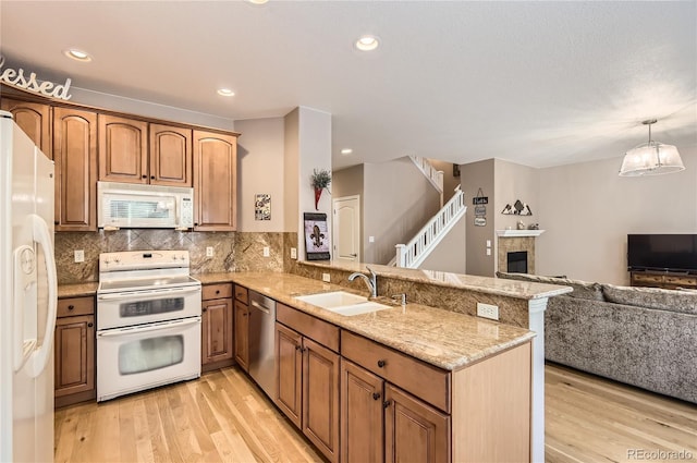 kitchen with a sink, open floor plan, white appliances, light wood-type flooring, and a peninsula