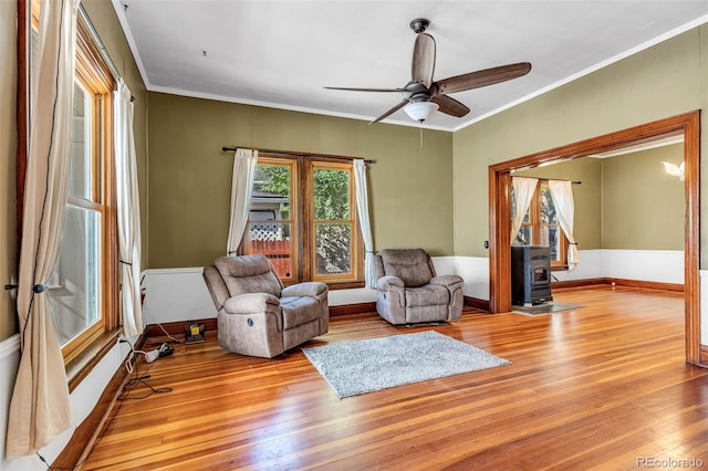 living room featuring ceiling fan, light wood-type flooring, crown molding, and a wood stove