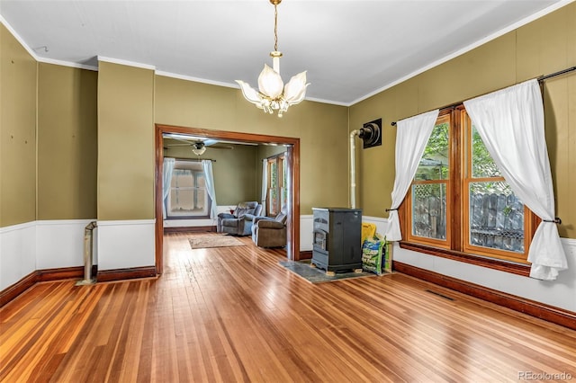 interior space featuring ceiling fan with notable chandelier, wood-type flooring, ornamental molding, and a wood stove