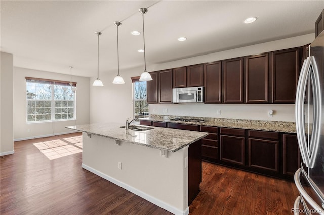 kitchen with dark brown cabinetry, a breakfast bar area, appliances with stainless steel finishes, dark wood-type flooring, and a sink