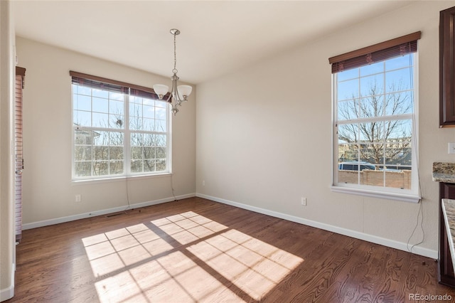 unfurnished dining area with a notable chandelier, baseboards, wood finished floors, and a healthy amount of sunlight