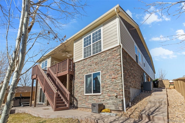 rear view of house with ceiling fan, cooling unit, fence, stairs, and stone siding