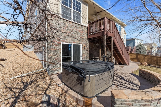 rear view of house with fence, stone siding, stairway, a patio area, and a hot tub