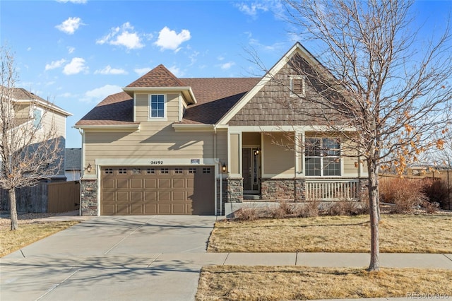 craftsman-style home featuring a porch, a shingled roof, fence, driveway, and stone siding