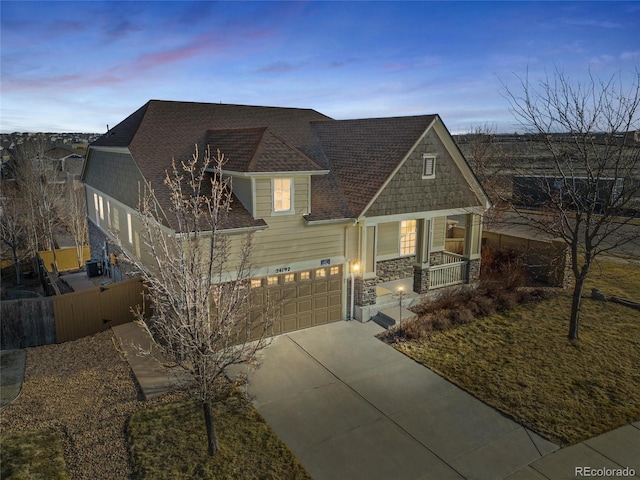 view of front of property featuring roof with shingles, a porch, fence, stone siding, and driveway