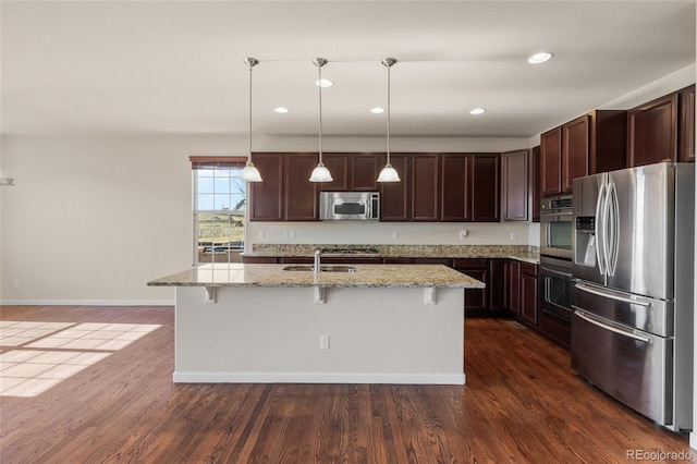 kitchen with dark wood-style floors, stainless steel appliances, dark brown cabinetry, a sink, and a kitchen bar