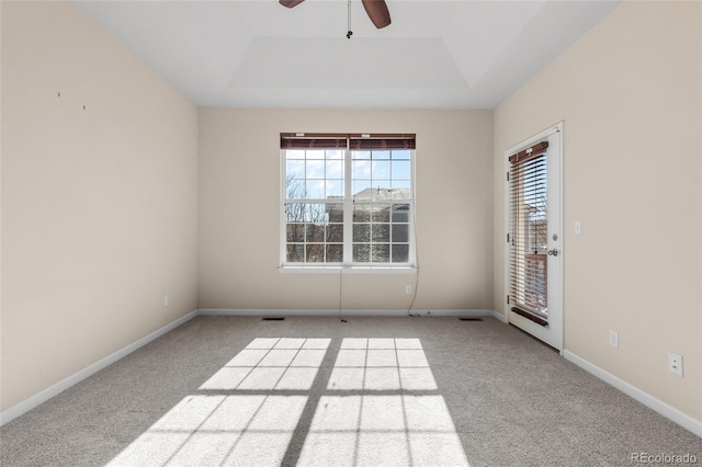 carpeted spare room featuring a raised ceiling, a healthy amount of sunlight, ceiling fan, and baseboards