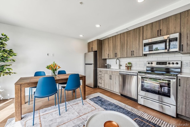 kitchen featuring decorative backsplash, sink, light hardwood / wood-style floors, and appliances with stainless steel finishes