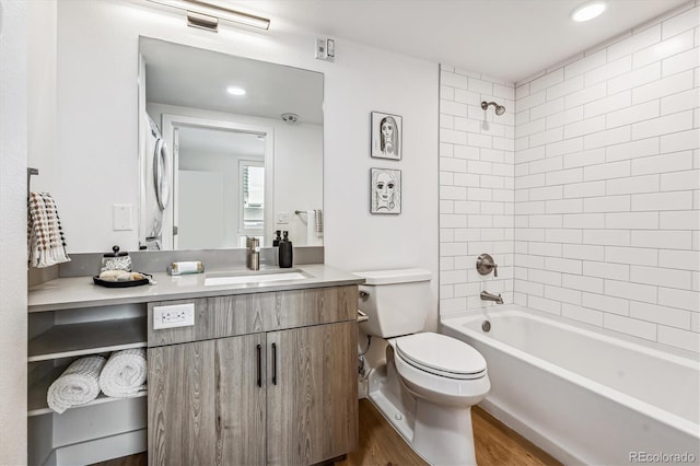 full bathroom featuring tiled shower / bath combo, wood-type flooring, stacked washer / drying machine, toilet, and vanity