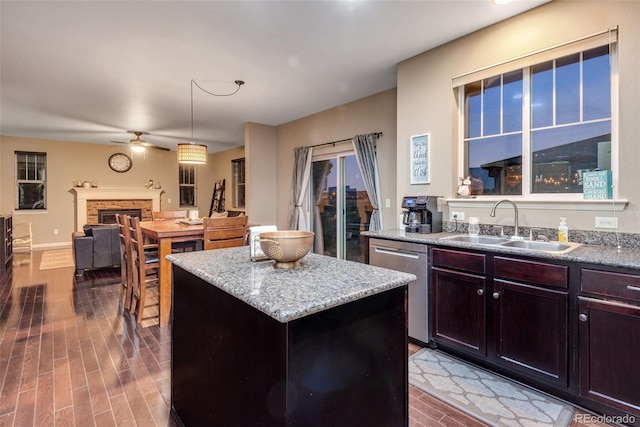 kitchen with a kitchen island, a brick fireplace, stainless steel dishwasher, sink, and decorative light fixtures