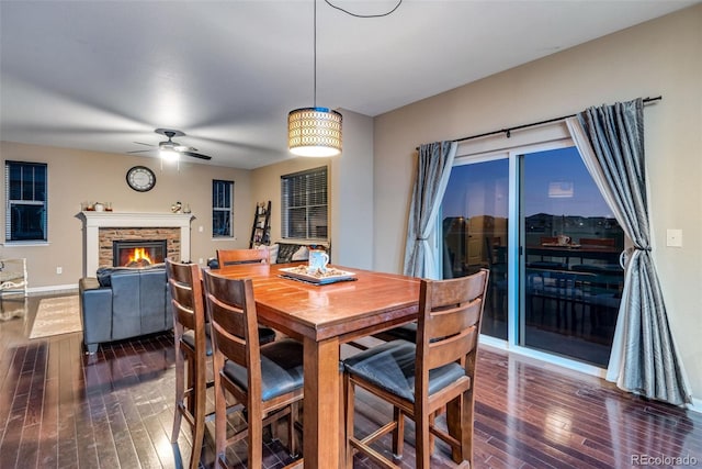 dining area featuring ceiling fan, dark hardwood / wood-style flooring, and a stone fireplace