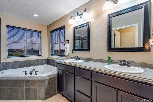 bathroom with tile patterned floors, tiled tub, vanity, and a textured ceiling