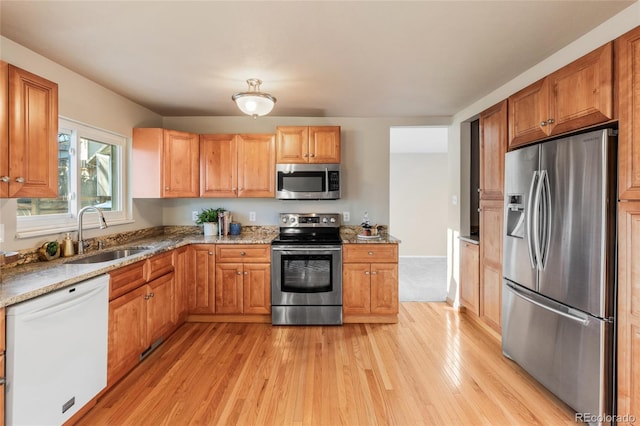 kitchen with light stone counters, stainless steel appliances, light wood-style flooring, brown cabinetry, and a sink