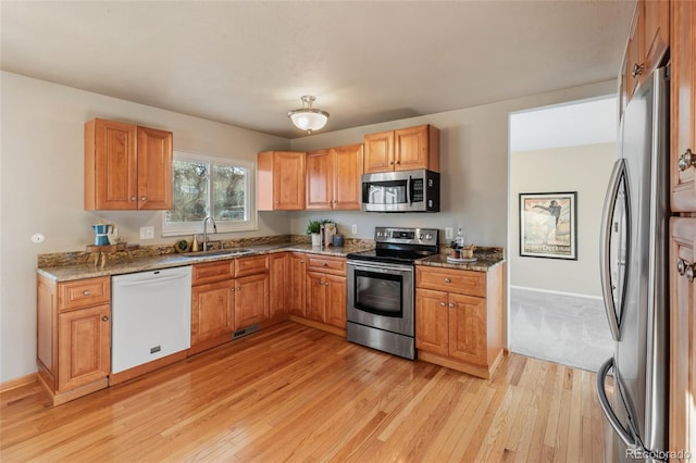 kitchen featuring light wood-type flooring, light stone counters, stainless steel appliances, and a sink