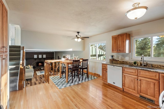 kitchen with stone counters, white dishwasher, a sink, and light wood-style flooring