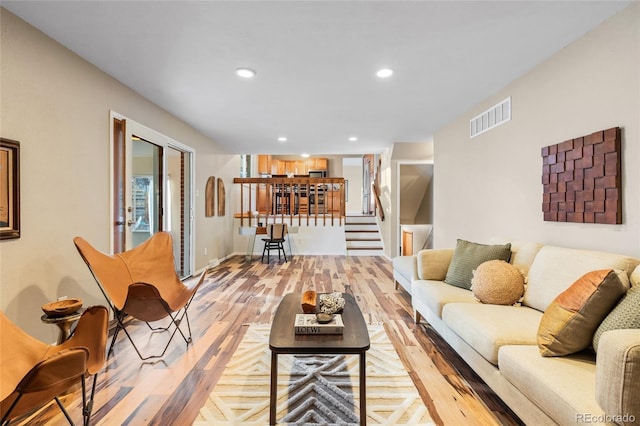 living area featuring visible vents, baseboards, light wood-style flooring, stairs, and recessed lighting