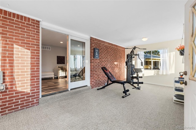 exercise room with carpet, visible vents, and brick wall